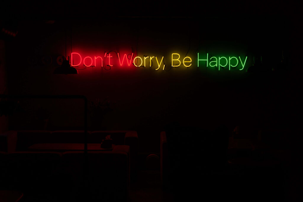 Glowing neon sign saying Don't Worry Be Happy in red yellow and green on dark background wallpaper