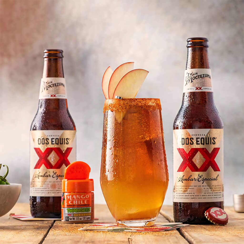 Two Dos Equis Ambar Especial bottles with chili rimmed apple cocktail and mango chile seasoning Wallpaper