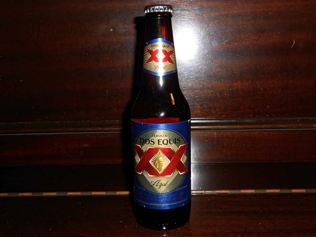 Dos Equis beer bottle on dark wood background with vibrant red and gold label details Wallpaper