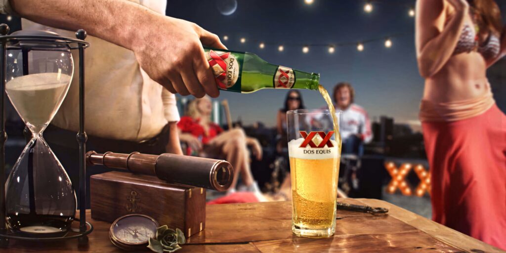 Dos Equis beer poured in branded glass at rooftop party with festive lights and warm golden tones Wallpaper
