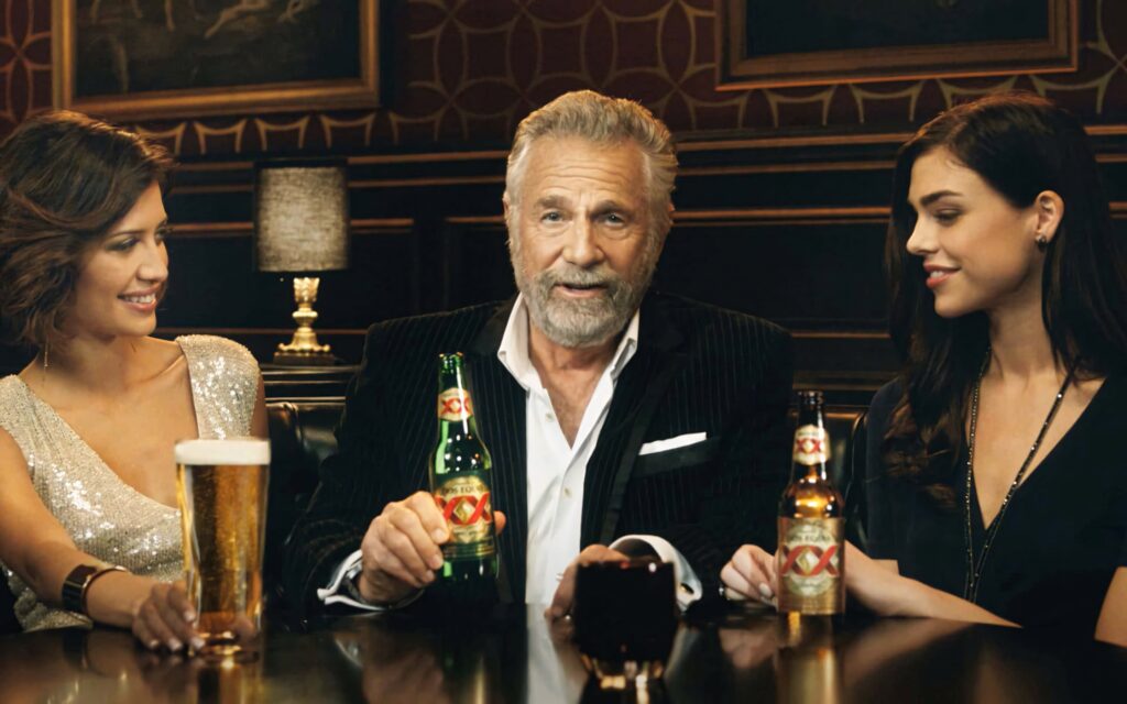 Stylish Dos Equis ad with distinguished man and two models in upscale bar highlighting luxury Wallpaper