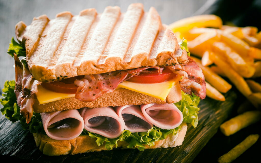 The Ultimate Fast Food Feast: HD Wallpaper showcasing a Mouthwatering Double Ham Sandwich and Sausage, with a Side of Scrumptious French Fries!