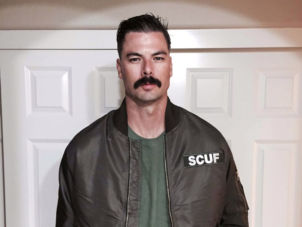 Dr DisRespect in green jacket with SCUF patch standing confidently by white panel door wallpaper