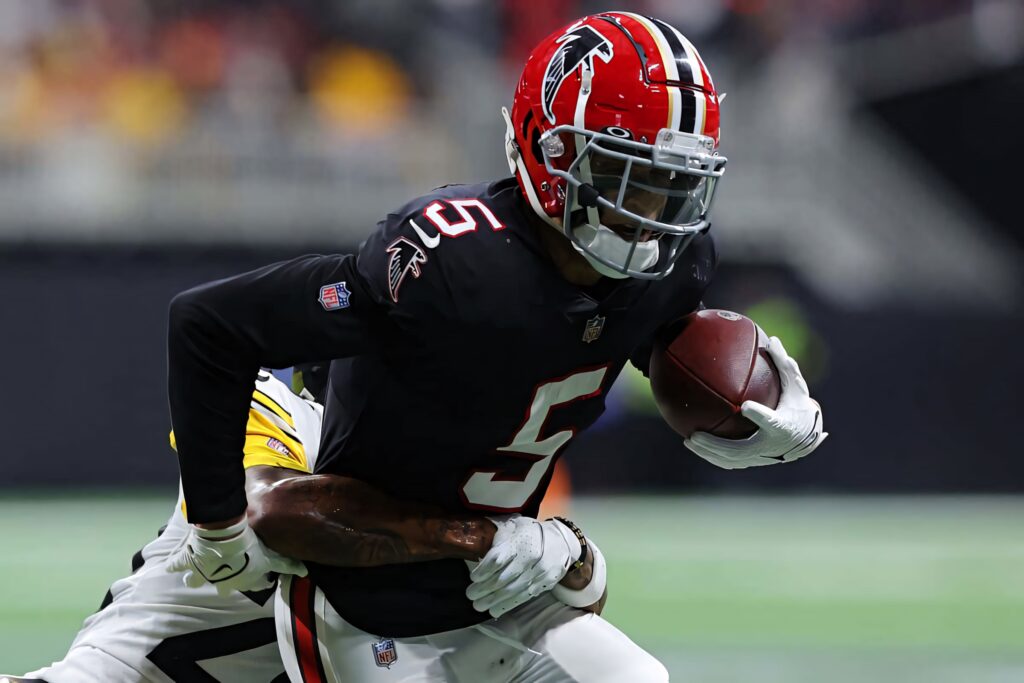 Drake London sprinting with football in Atlanta Falcons uniform breaking away from defender in stadium Wallpaper