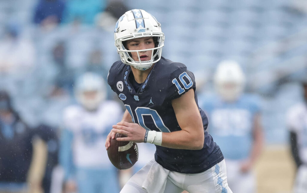 Quarterback Drake Maye in action focused on football field with dynamic blue and white tones wallpaper