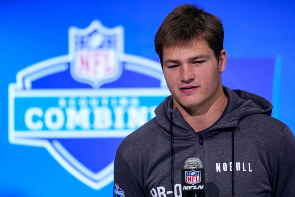 Drake Maye NFL Combine interview wearing dark hoodie holding microphone blue background wallpaper
