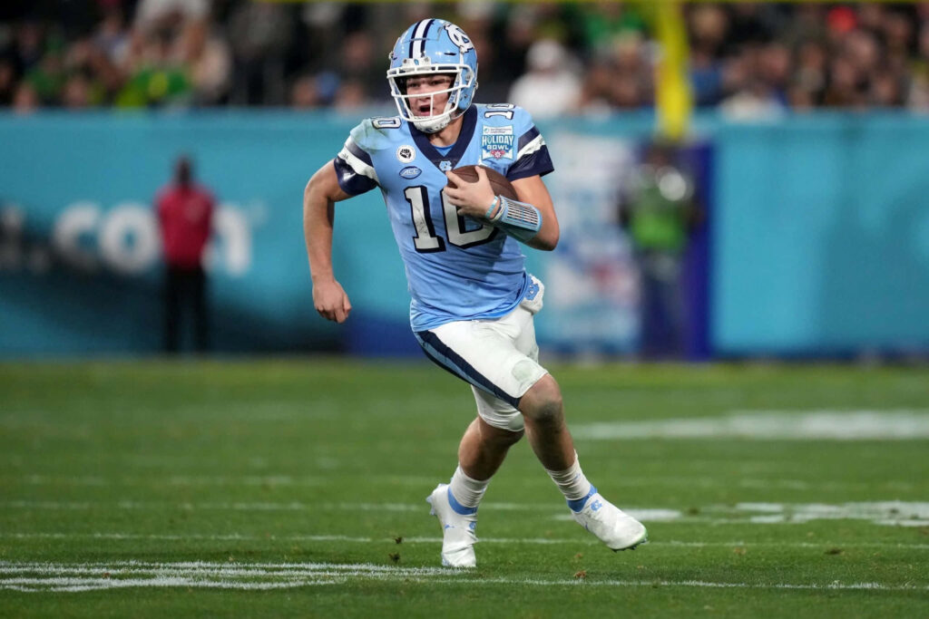 Drake Maye in light blue UNC Tar Heels uniform sprinting on field under stadium lights wallpaper