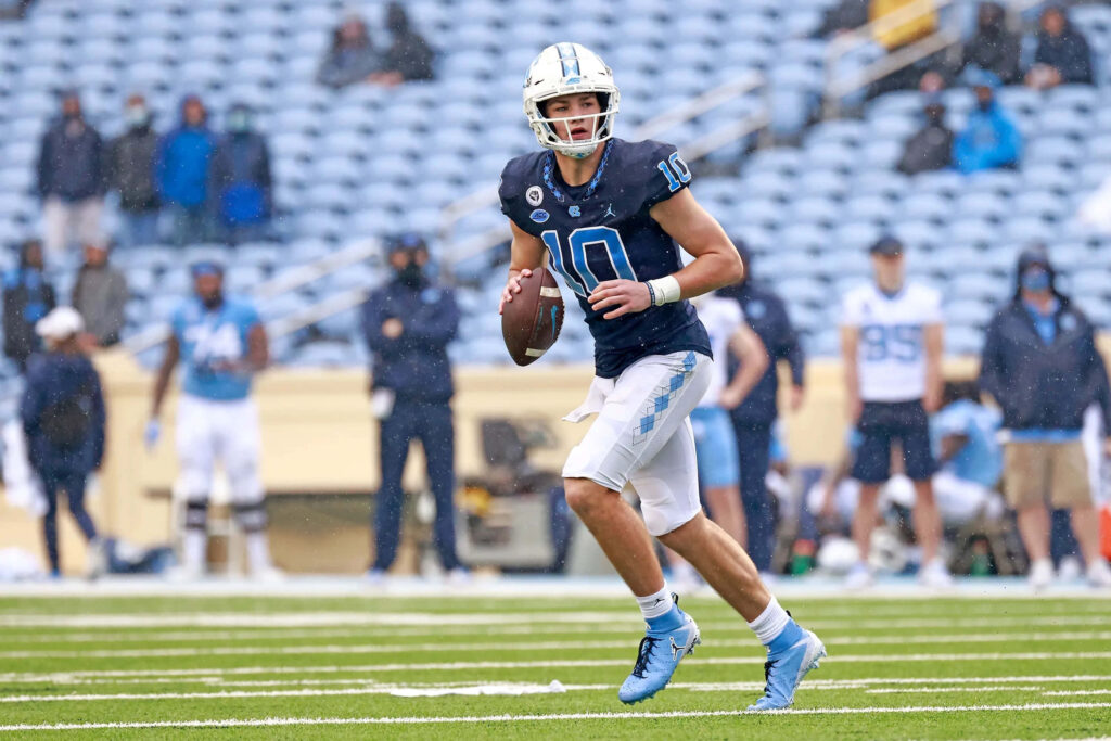 Quarterback Drake Maye in blue white jersey number 10 prepares to throw on green football field Wallpaper