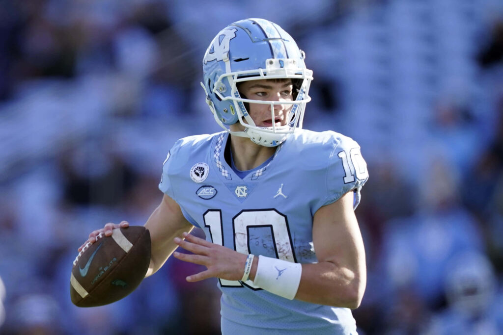 Drake Maye UNC quarterback in powder blue uniform mid-action with dynamic stadium lighting wallpaper