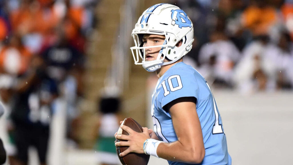 Drake Maye UNC quarterback number 10 in light blue uniform gripping football under stadium lights Wallpaper