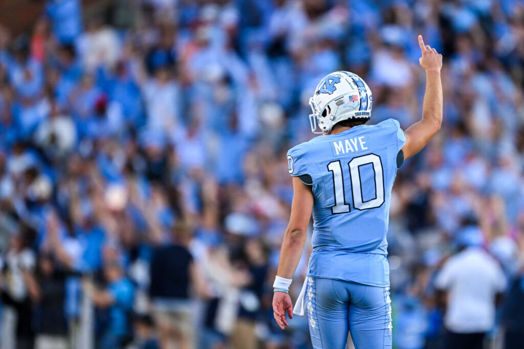 Drake Maye in Number 10 jersey raises victory on UNC Tar Heels field with stadium crowd background Wallpaper