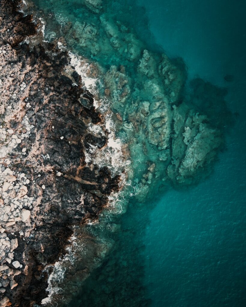 Aerial view of rocky coastline meeting clear turquoise sea with natural textures and patterns Wallpaper