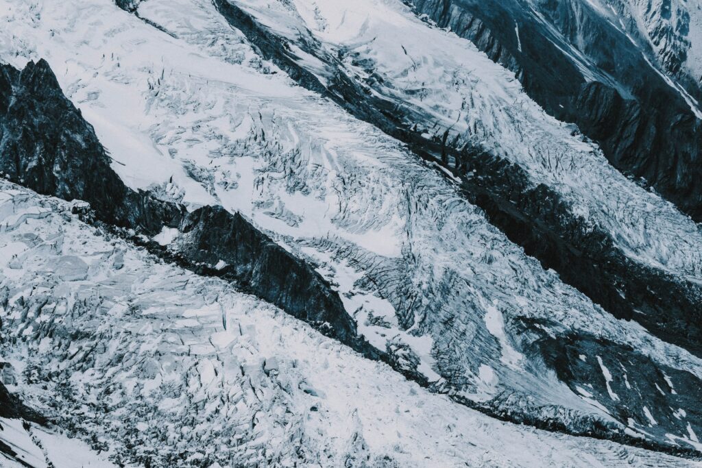 Aerial view of glacier with rugged rocks icy surfaces and layered snow in blue and white tones Wallpaper