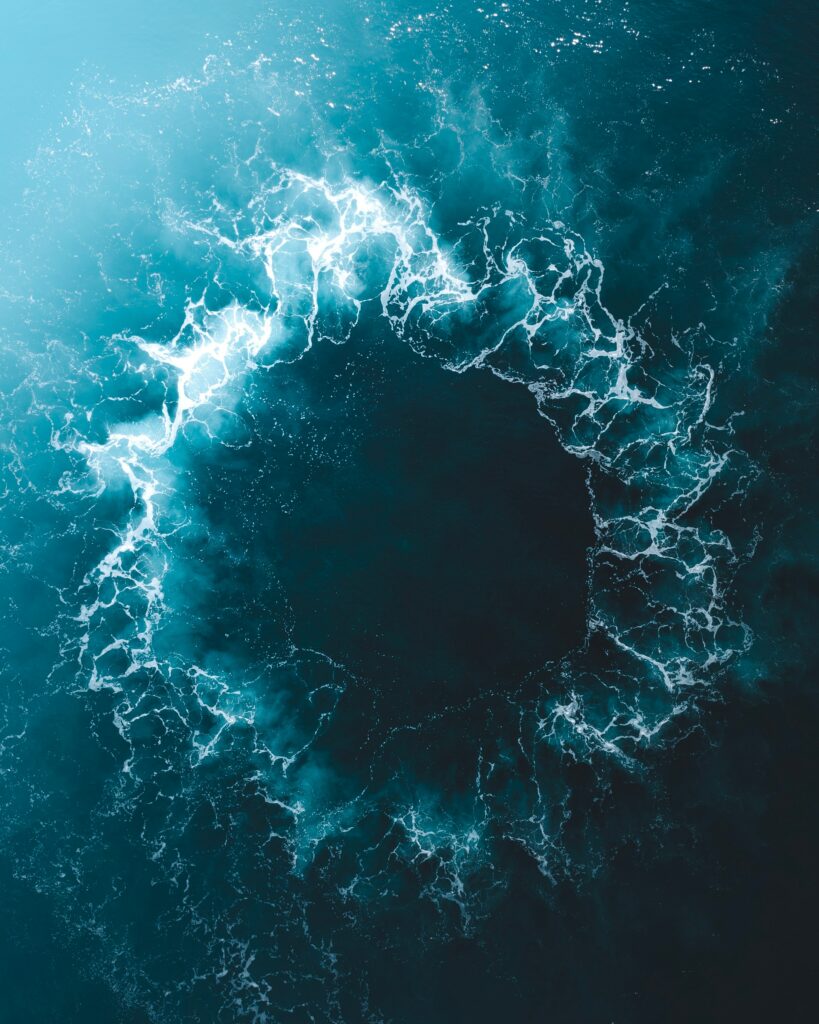 Aerial view of vibrant blue ocean with circular splash pattern and dynamic white waves wallpaper