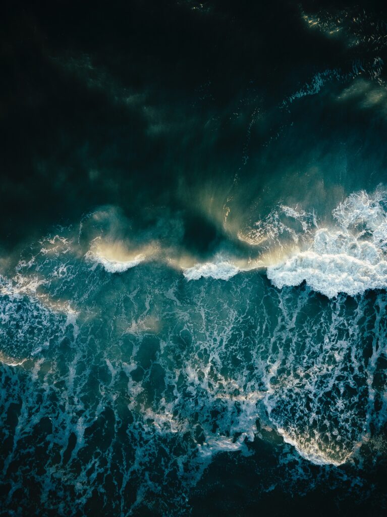 Aerial view of ocean waves crashing surf with deep blue and turquoise foamy seascape wallpaper