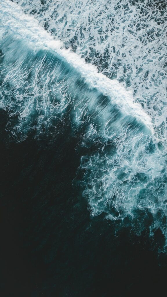 Aerial view of powerful ocean waves crashing over deep blue water with white foamy surf wallpaper