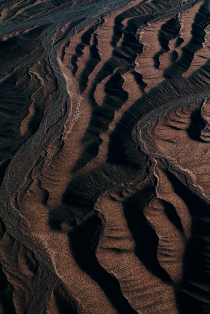 Aerial view of dark sand dunes with rugged ridges and deep shadows creating textured background Wallpaper