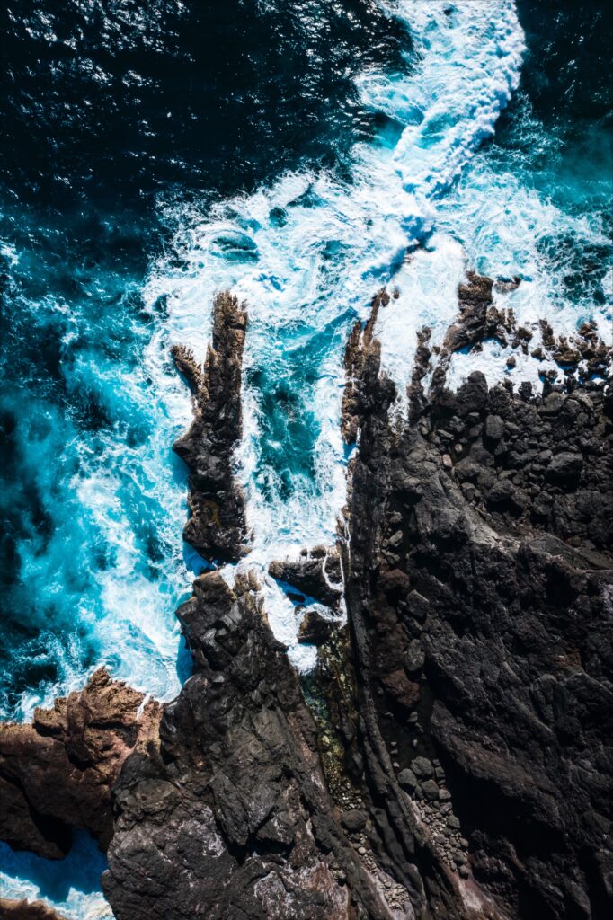 Aerial view of deep blue ocean waves crashing white surf on rugged rocky coastline seascape wallpaper