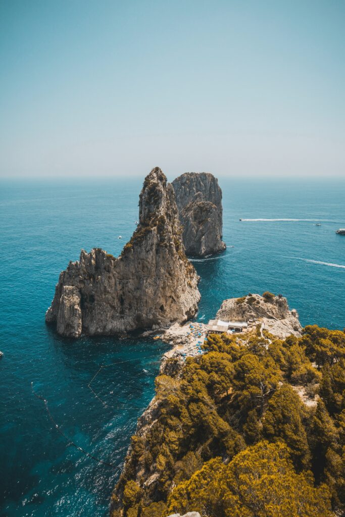 Aerial view of rocky coastal formations with lush greenery and deep blue ocean under clear sky Wallpaper