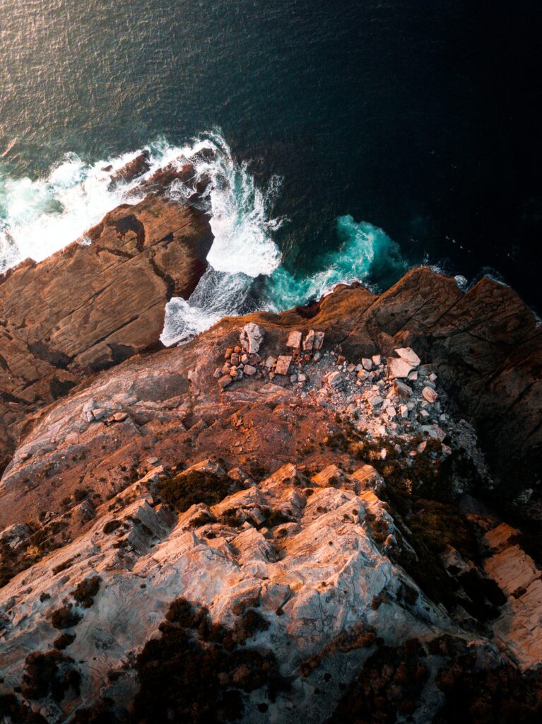 Aerial view of rugged cliffs crashing waves deep blue sea dramatic coastal scenery wallpaper background