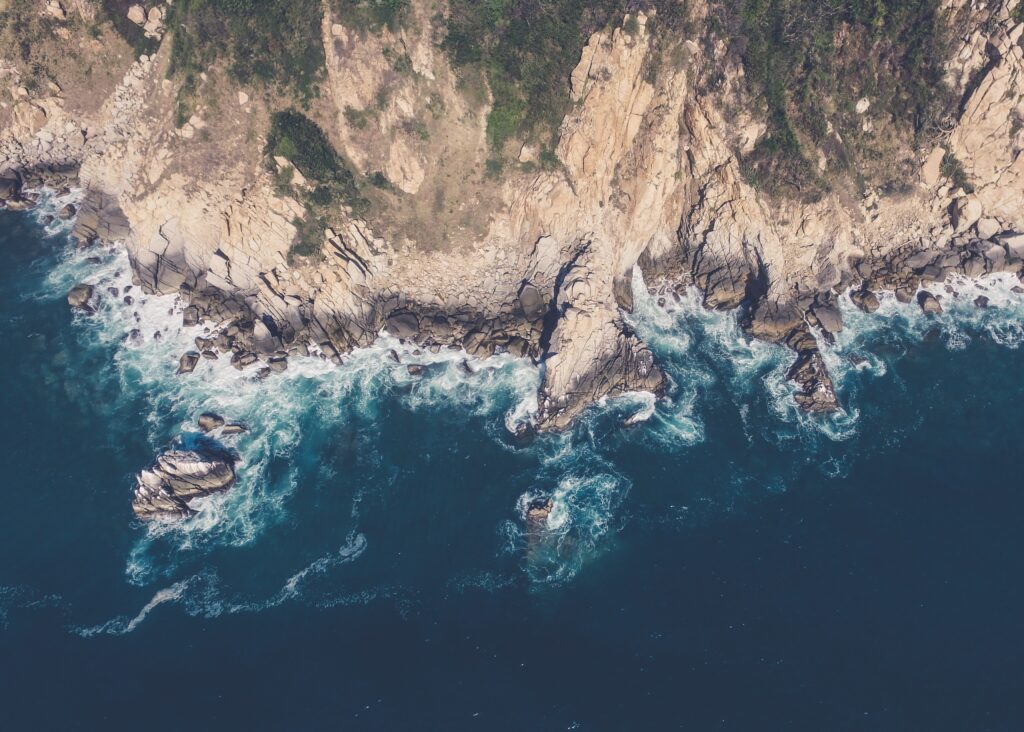 Aerial view of rugged island coastline with crashing waves rocky cliffs and deep blue sea wallpaper