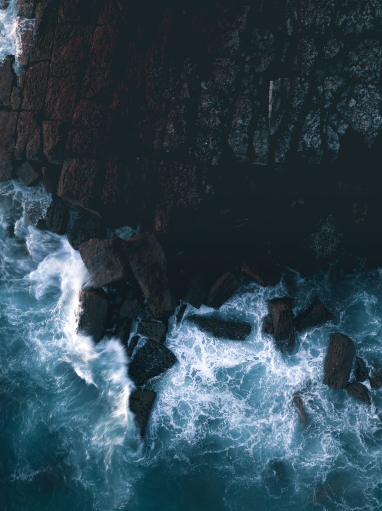 Aerial view of rugged rocky cliffs with foamy blue ocean waves crashing dramatic natural wallpaper