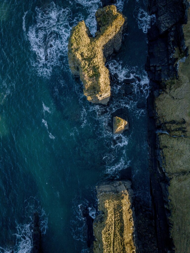 Aerial view of rugged sea rocks with crashing waves and deep blue coastal waters wallpaper background