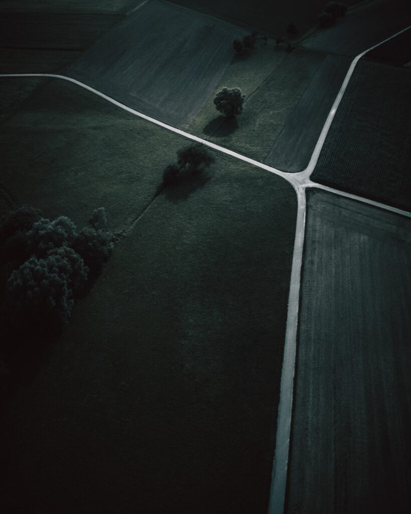 Aerial view of dark moody fields with winding roads and scattered trees minimalist wallpaper background