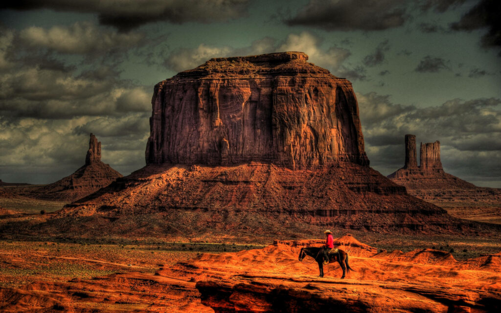 Massive Arizona desert rock formation with lone horseback rider under moody sky wallpaper.