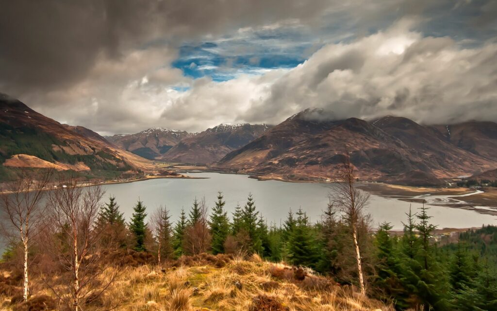 Autumn landscape with fir trees lake mountains swirling clouds and sunlight vibrant nature scene Wallpaper