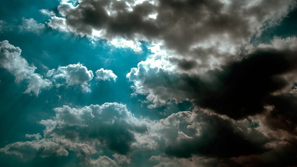 Dramatic azure sky with dynamic clouds and sunlight beams creating light and shadow contrast Wallpaper
