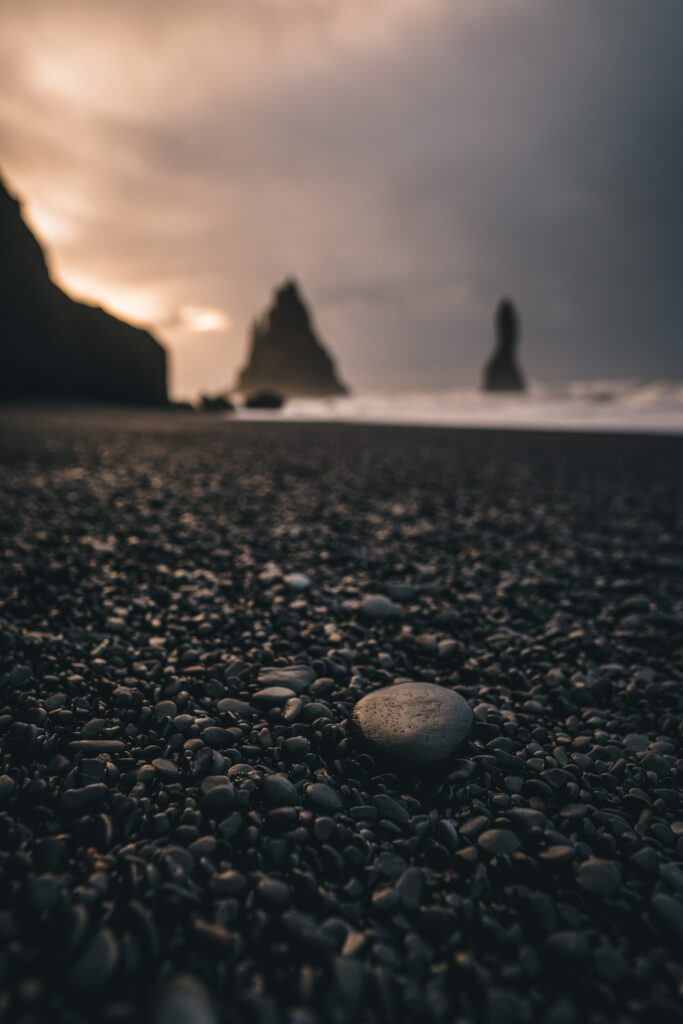 Dramatic sunset beach with smooth black rocks and towering formations under golden sky Wallpaper