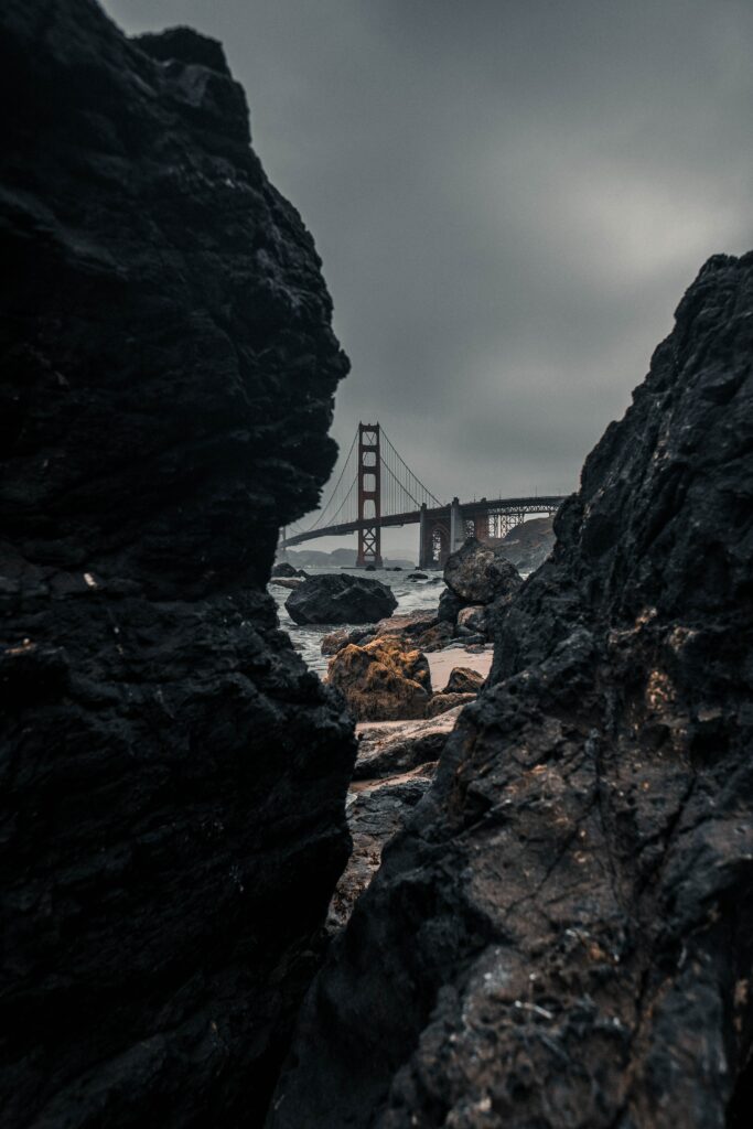 Dramatic black rocks framing river bridge under moody cloudy sky cinematic wallpaper background