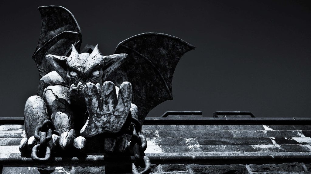 Black and white ancient stone gargoyle with wings spread on brick wall against moody sky Wallpaper