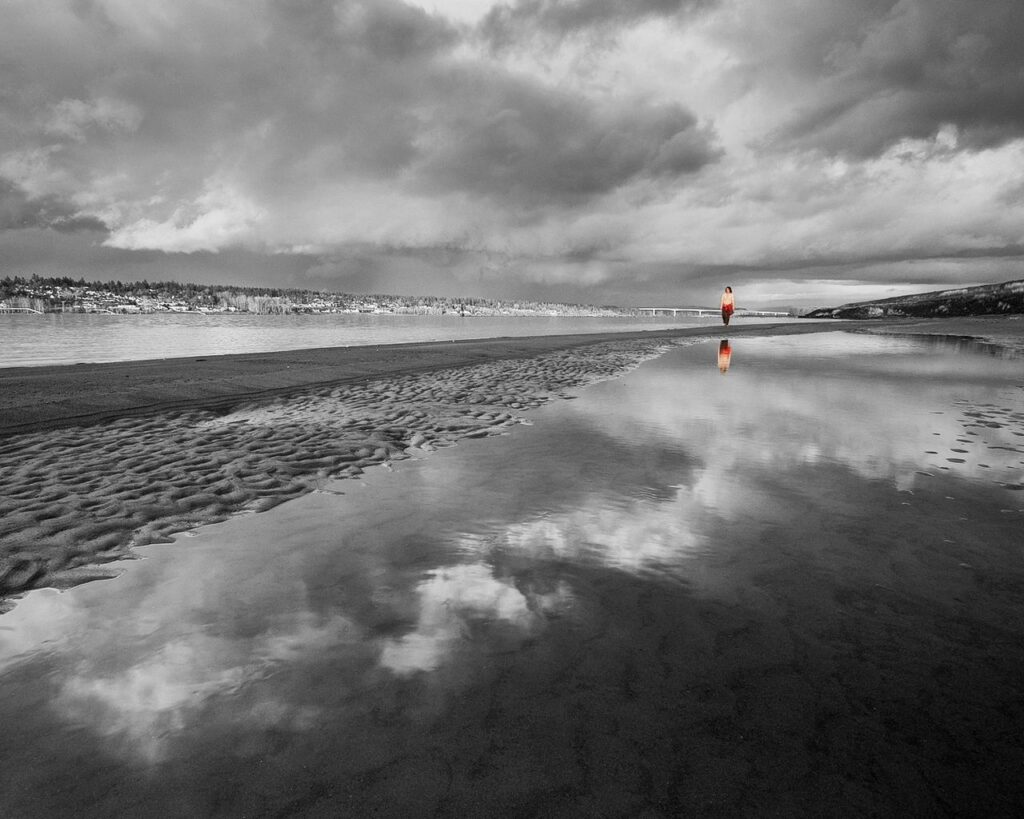 Black and white beach wallpaper with rippled sand reflective water cloudy sky and lone silhouette