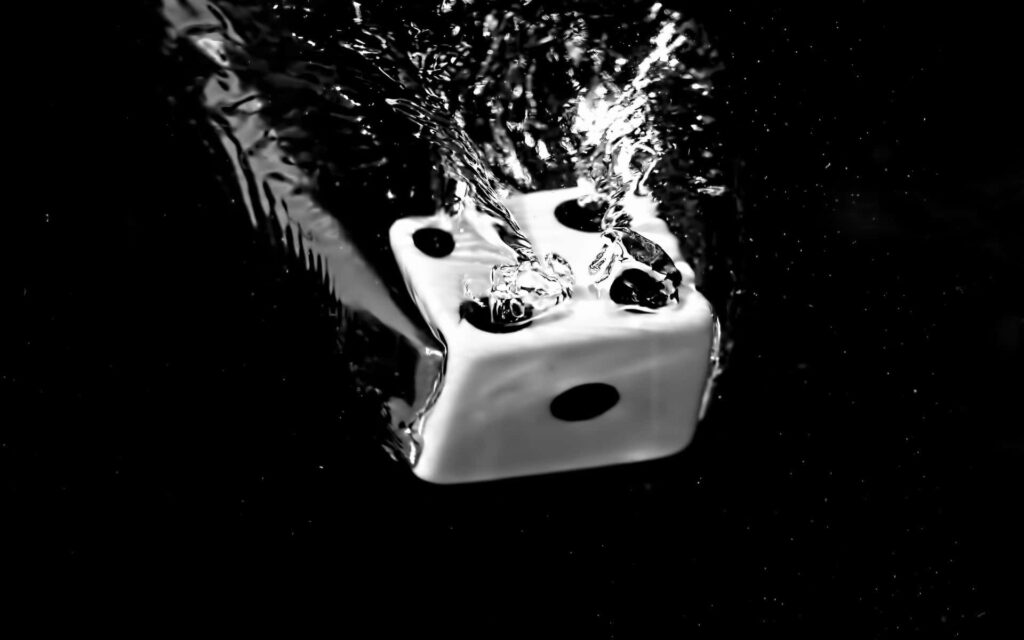 White die dropping into water with splashes and ripples black and white dramatic wallpaper background