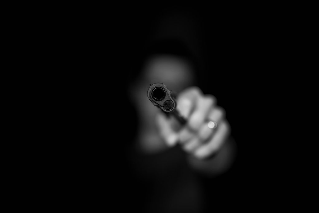 Black-and-white high-contrast handgun focused aiming at viewer blurred dark background wallpaper