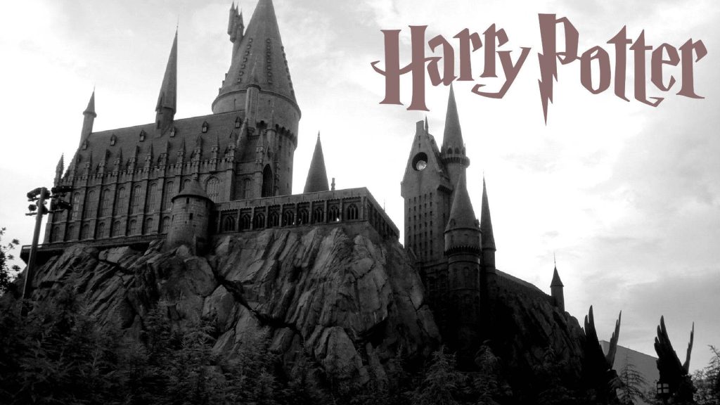 Black and white Hogwarts Castle wallpaper with moody sky and iconic Harry Potter logo background