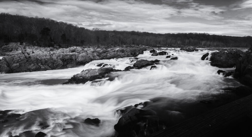 Black and white river flowing over rugged rocks with wild forest and textured sky wallpaper background