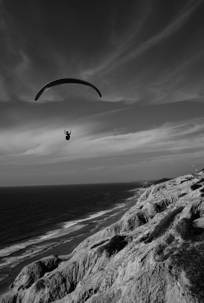 Striking Black and White Coastal Wallpaper with Skydiver Above Cliffs