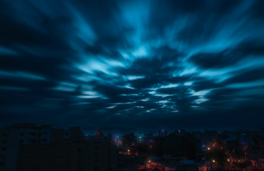 Dramatic night sky with vibrant blue streaking clouds over quiet cityscape cinematic wallpaper
