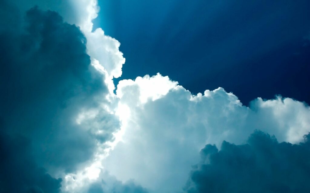 Dramatic blue sky with bright white clouds and radiant light beams creating serene wallpaper