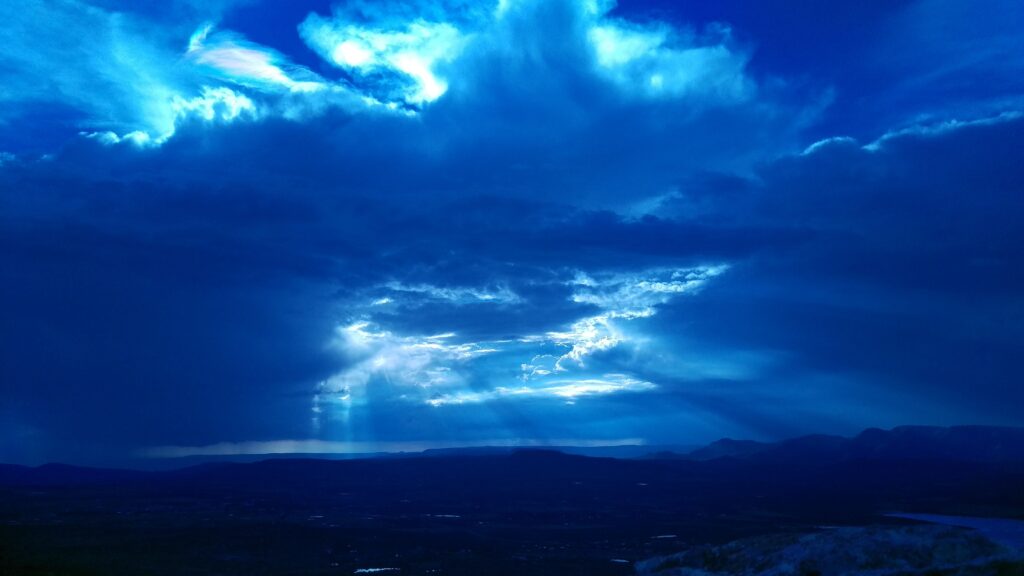 Vivid blue sunset with light rays through thick clouds over serene mountain horizon wallpaper