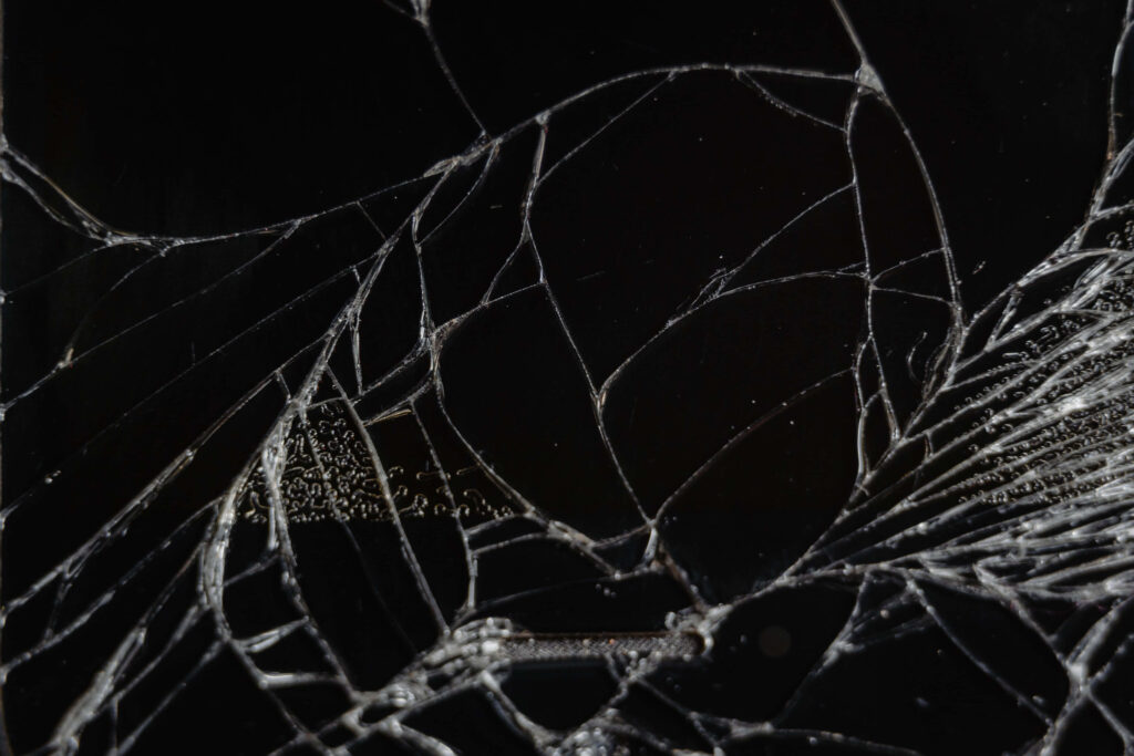 Shattered glass pieces on black surface with intricate cracks and sharp reflections background Wallpaper