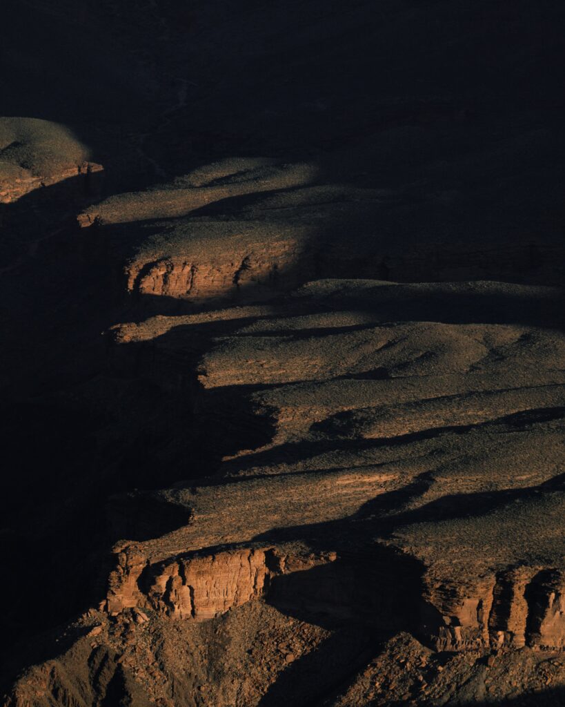 Dramatic canyon landscape with layered rock formations and cliffs in warm sunlight and shadows Wallpaper