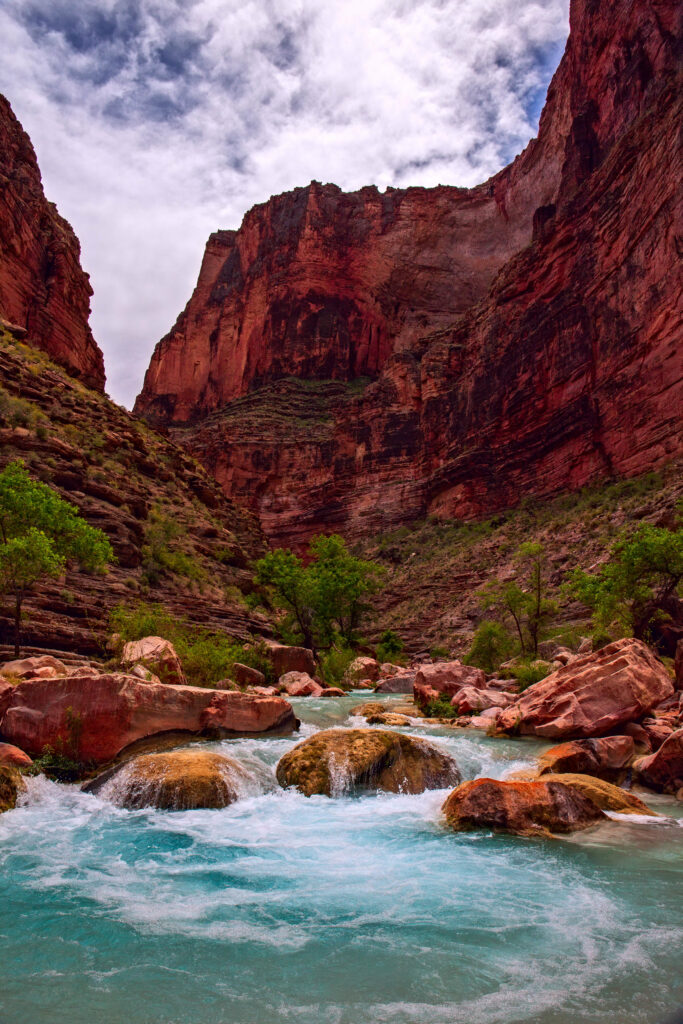 Dramatic red canyon cliffs green trees and turquoise river under cloudy sky nature wallpaper background