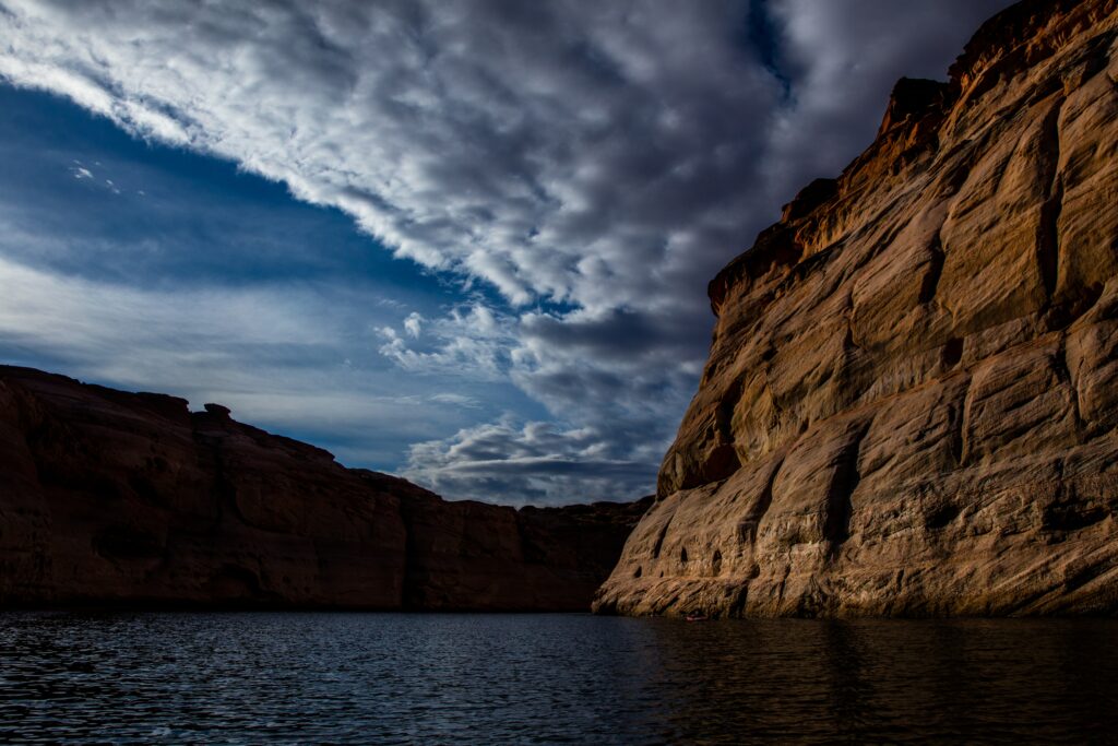 Dramatic canyon landscape with towering cliffs and tranquil lake under a vivid cloudy sky wallpaper