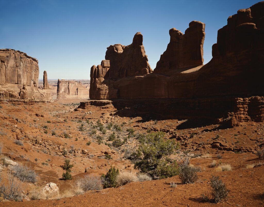 Dramatic canyon landscape with towering stone formations warm desert tones and green vegetation Wallpaper