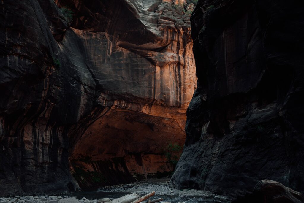 Dramatic canyon with towering textured rocks winding river and sunlit glowing orange cave walls wallpaper