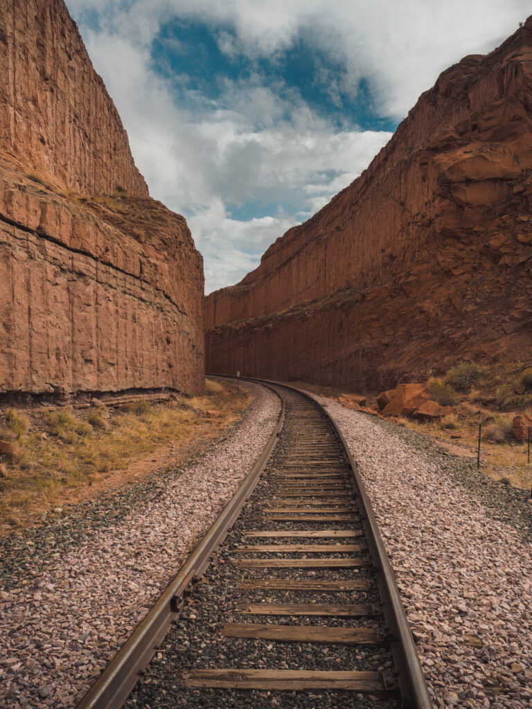 Dramatic railway curving through rugged canyon with towering red rock walls and cloudy sky wallpaper